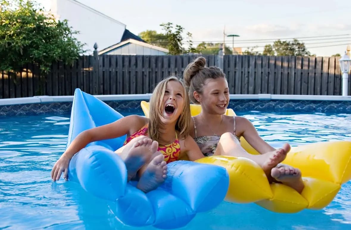 Two girls sitting on floats in an above ground pool